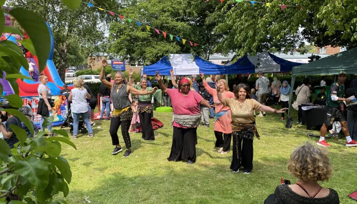 A group of six people dancing at a festival in a green space 
